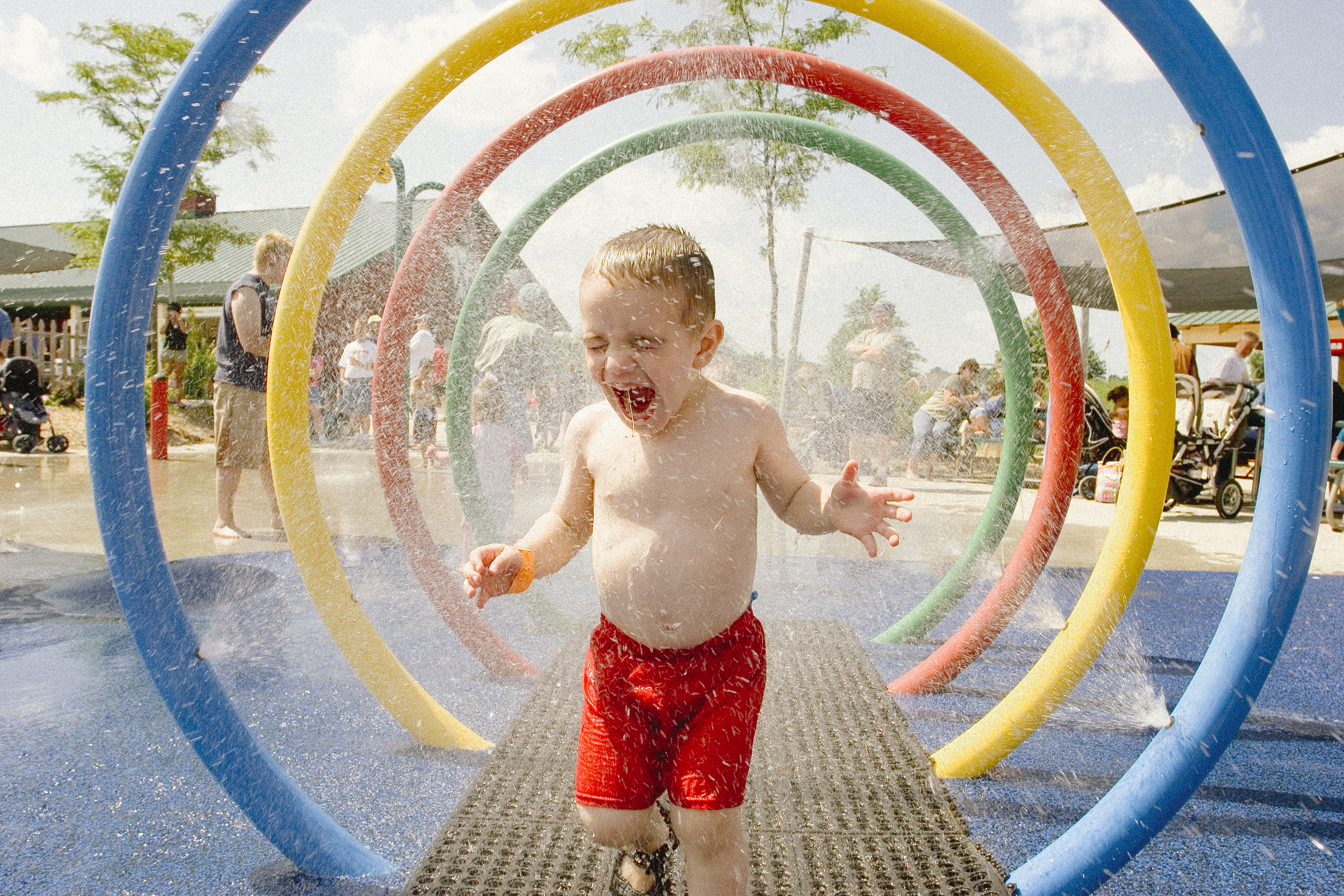 Young laughing boy runs through water park sprinklers