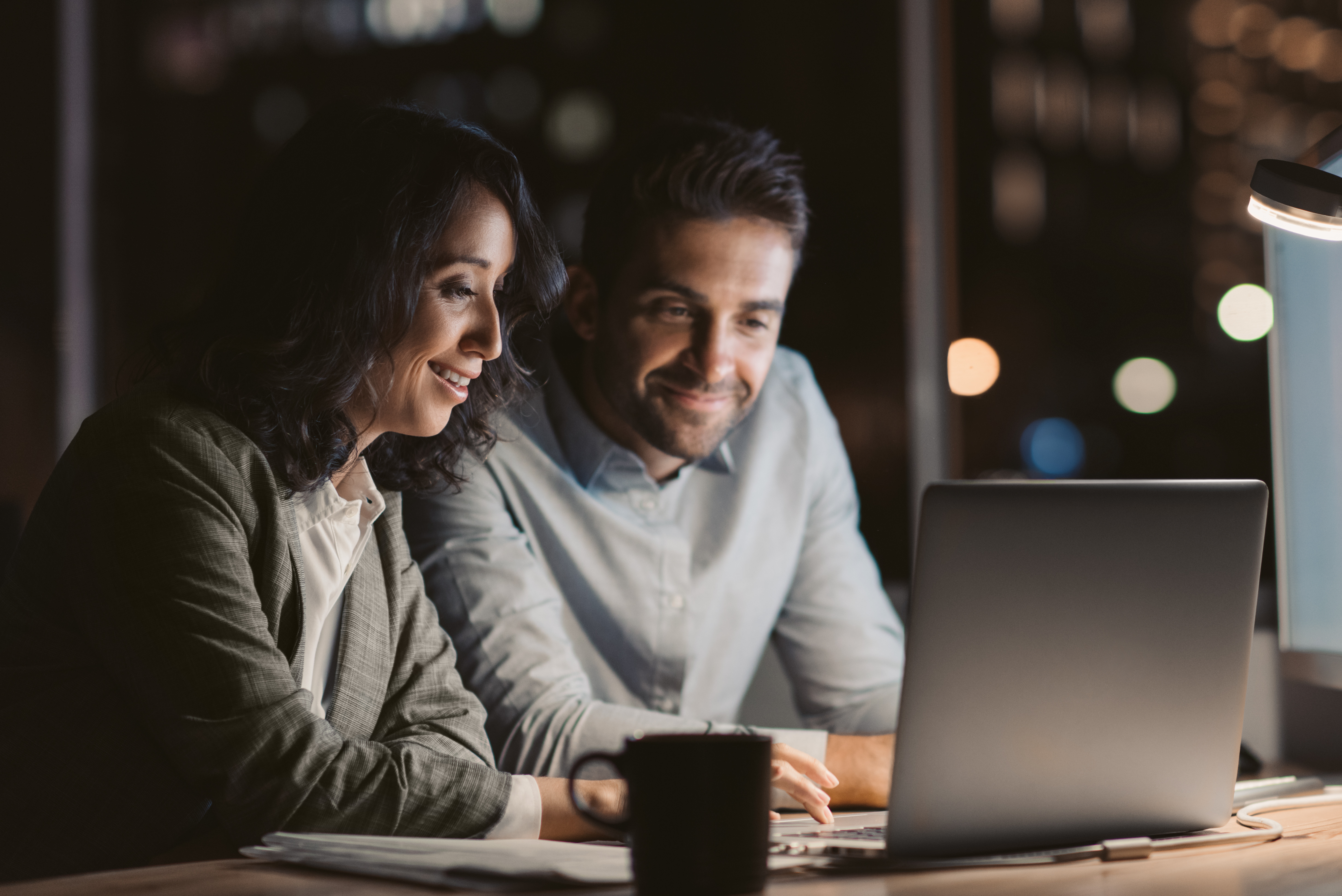 Two smiling office colleagues using a laptop while working