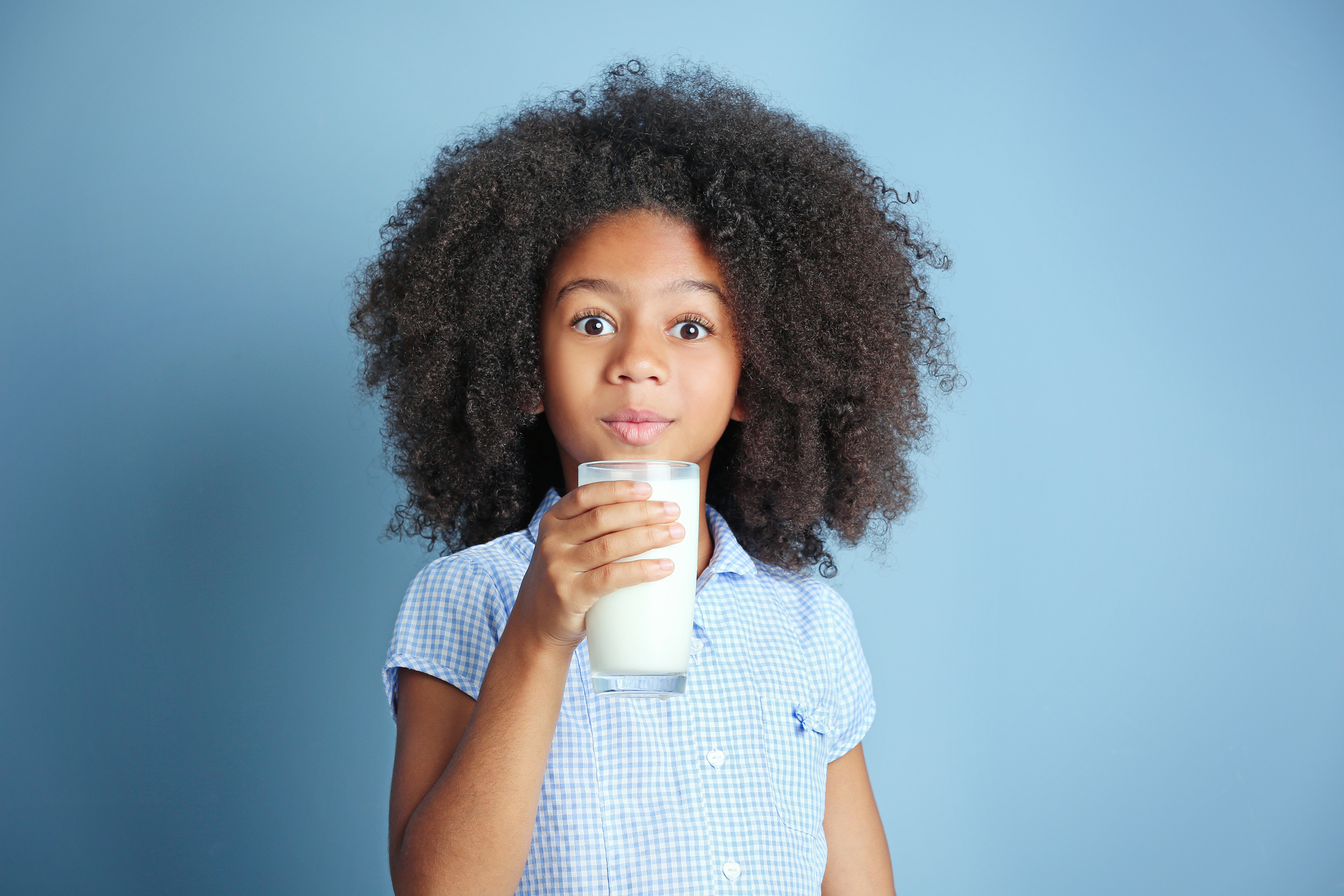 Cute curly African-American girl drinking milk on a blue background