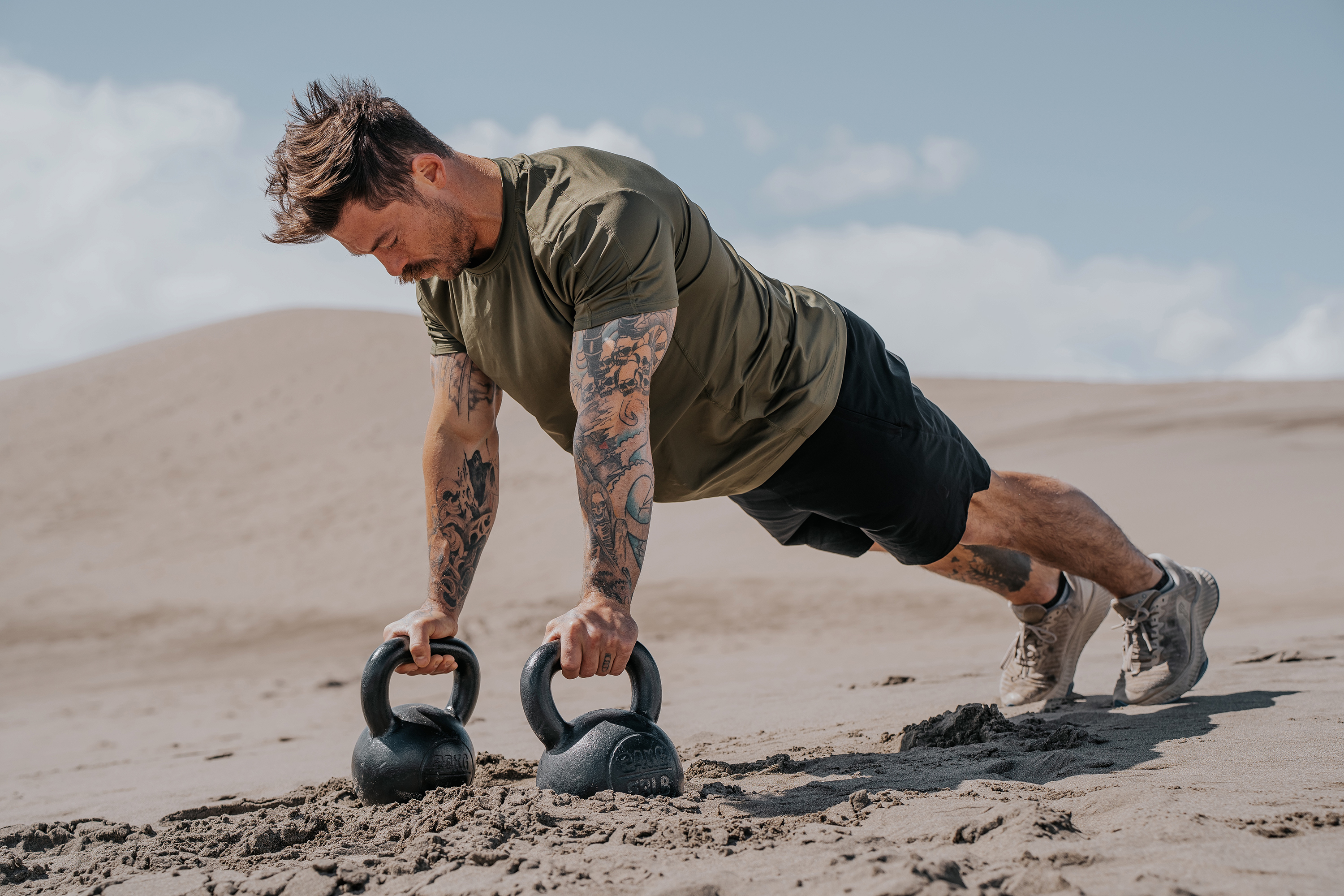 LINEAR Clothing model wearing Baseline Series Shirt and shorts doing kettle bell pushups in the sand
